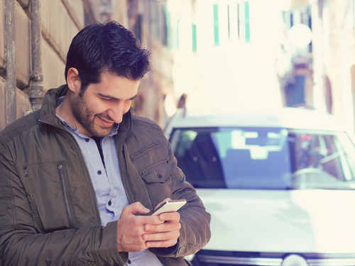 man looking at cell phone with car in background