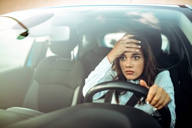Woman in white shirt expressing frustration while driving