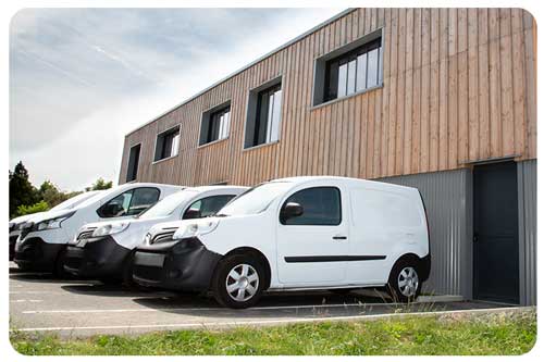 Several row of white commercial cars vans and trucks parked in parking lot