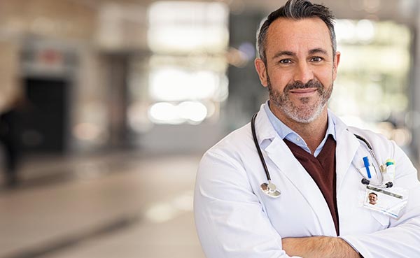 a male doctor is smiling with his arms crossed in the hospital hallway