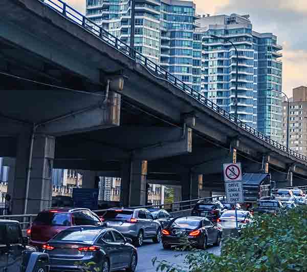 Traffic moving beneath an elevated roadway in a downtown area with modern high-rise buildings.