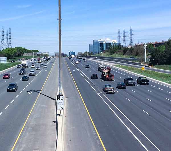 Traffic travelling in both directions on a wide multi-lain highway under a clear blue sky.