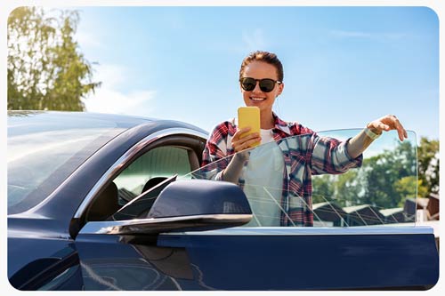 female car driver stands next to her car and using apps.
