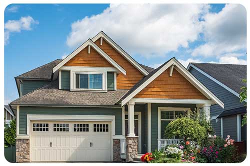 home with a charming exterior, featurimg a combination of wood paneling and stonework around the garage and front porch.