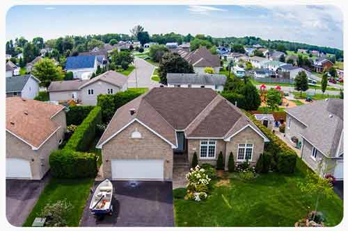 Looking down on a brick house with a boat in the driveway and other homes in neighborhood