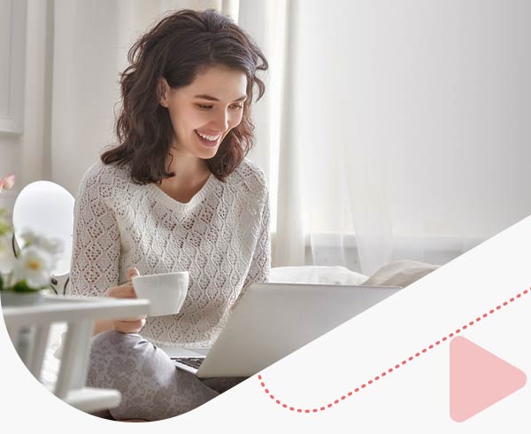 Young woman working on a laptop sitting on the bed in the house.