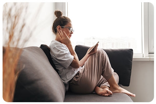 Woman using cellphone while sitting on sofa at living room