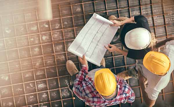 three people on a construction site looking down on a blueprint