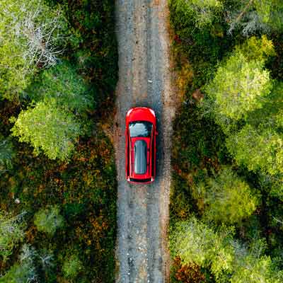 red car driving through a road with trees