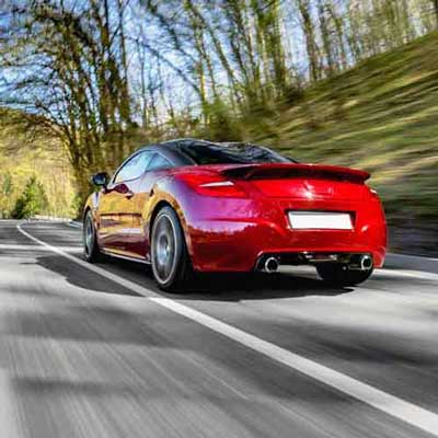 red car driving along a roadway 