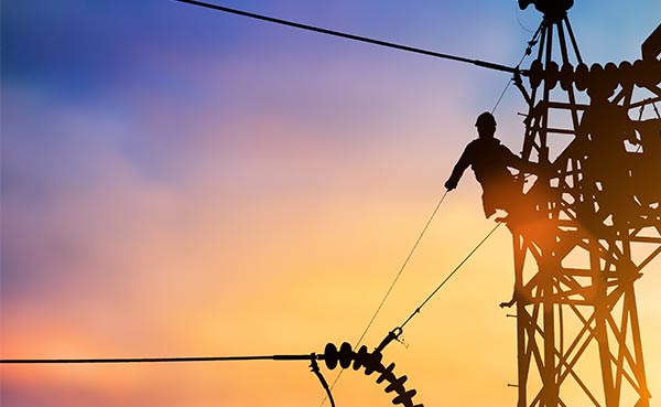 Electrician on power lines at sunset, safety insurance