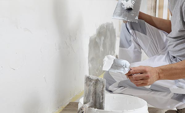 painter takes plaster from bucket to paint the wall