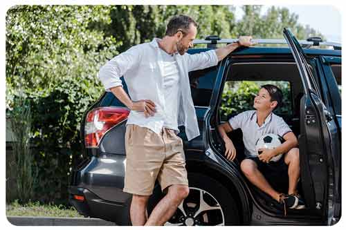 father standing with hand on hip near car and looking at son