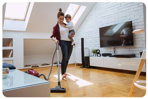 young mother holding baby and vacuuming