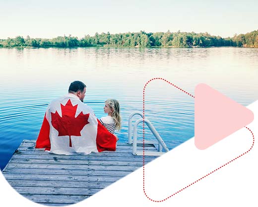 father and daughter wrapped in large Canadian flag sitting on wooden pier by lake