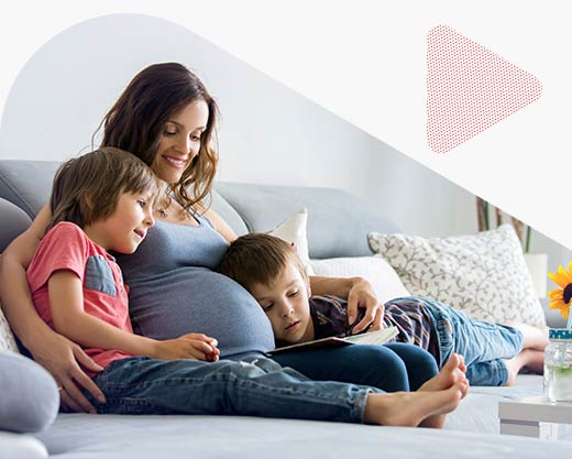 a pregnant woman, reading a book at home to her two boys