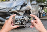 Person taking picture of the front of a damaged gray car after an accident