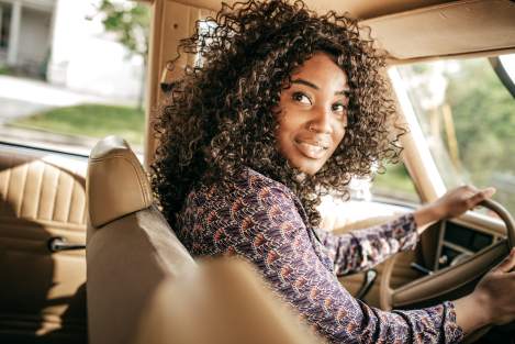 black woman driving a car looking backwards