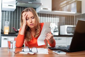 stressed woman looking at bills and laptop
