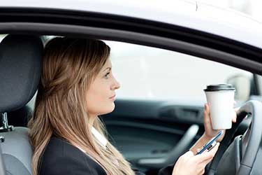 Women with a phone and coffee in her hands while driving