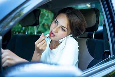 Women driving while distracted in by putting on makeup and using the phone