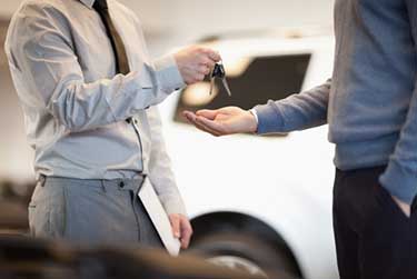 Two men standing beside a white car, one is handing over car keys to the other