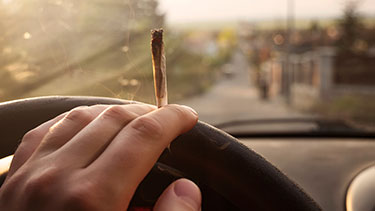 Person with a joint and hand on steering wheel