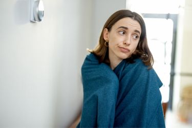 female with green blanket beside thermostat