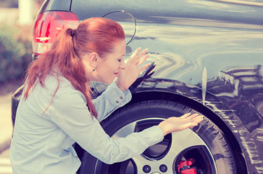 Frustrated woman looking at damage done to a black car 