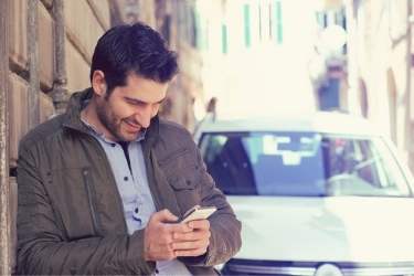 man looking at cell phone with car