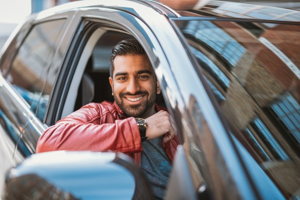 man wearing red jacket smiling while looking outside car window