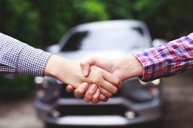 two people shaking hands infront of a car
