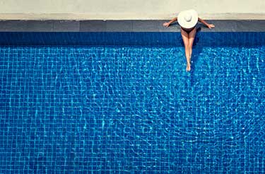 woman sitting on swimming pool edge with legs in the water