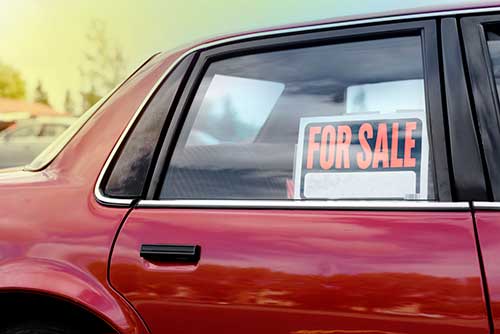 red car with for black and orange sale sign in window