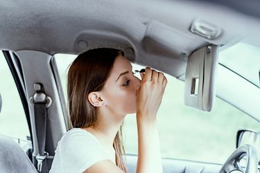 woman applying mascara behind the wheel