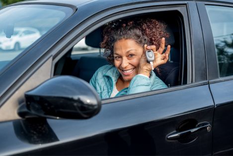 woman of colour holding car keys sitting inside car