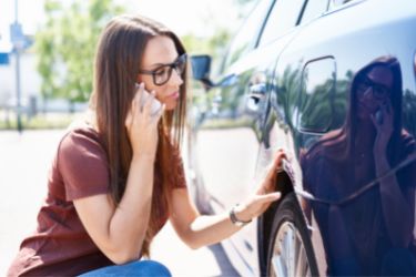 Brunette on the phone looking at her damaged vehicle