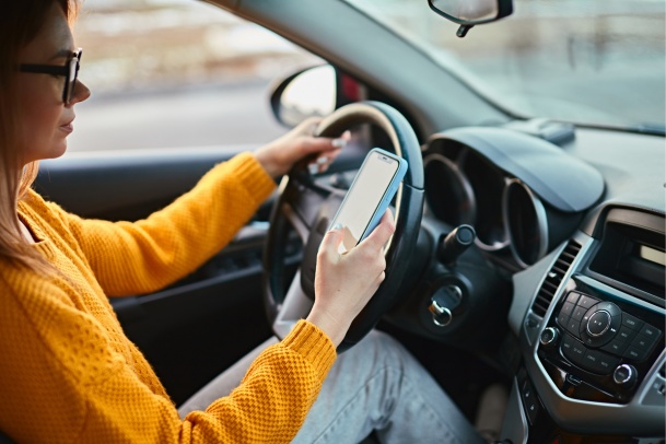 Woman wearing yellow sweater distracted driving looking at her phone in Alberta